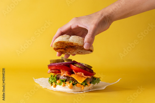 Hand picking up a feef burger with bacon on yellow background photo