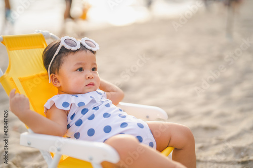 baby in white dress and sunglasses sit on the chair beach yellow color and relaxing and the wind blows in evening time and beautiful sunset light at the beach