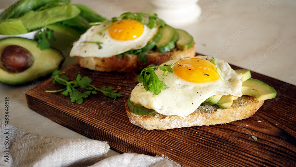 sandwich with egg and avocado on a wooden board and one in the background