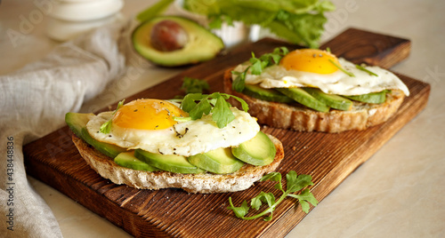 sandwich with egg and avocado on a wooden board and one in the background