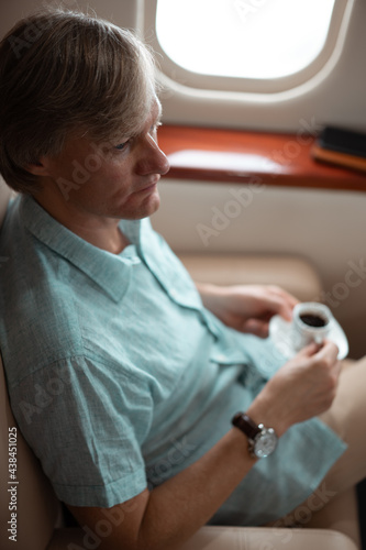 Attractive and successful businessman drinks coffee while sitting in the chair of his private jet