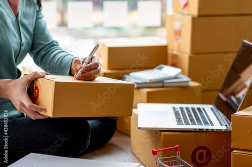 Close uo of female start up small business owner writing address on cardboard box at workplace.small business entrepreneur SME , working with box at home, Online selling, e-commerce, packing concept