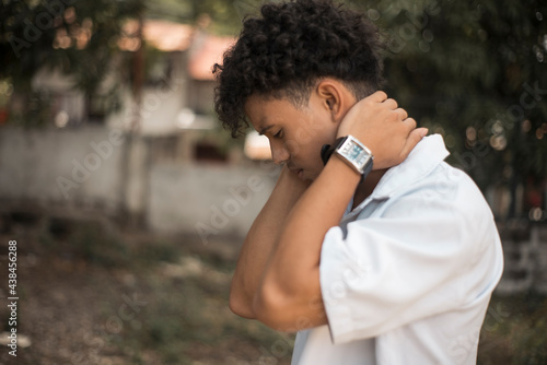A depressed Filipino African man holds his nape looking down. Young teenage issues and problems. Outside park background. photo