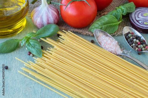 close up uncooked pasta and products on green background. dry spaghetti with vegetables and herbs on a wooden table.
