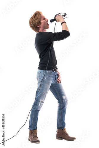 Loud energetic young singer singing loud and shouting on microphone. Full body length isolated on white background.