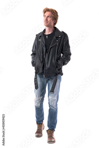 Cool stylish rocker in black leather jacket walking and looking away with hands in pockets. Full body length isolated on white background. © sharplaninac