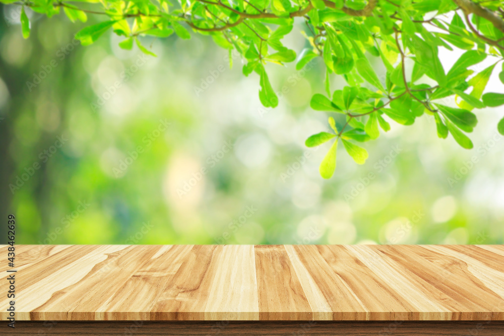 wooden table and green leaves background.