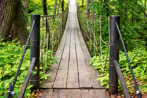 Suspension wooden bridge in the forest. Rope bridge suspended between two hills in the woods