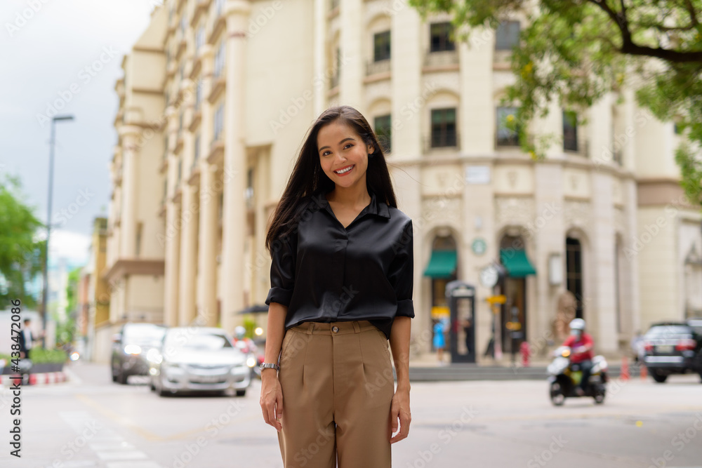 Portrait of beautiful Asian businesswoman smiling outdoors in city street while walking