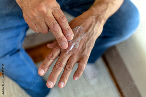 Cropped shot of unrecognized Caucasian man applying moisturizer to his hands. Cropped shot of an unrecognizable man applying lotion. Man applying hand cream at home, close up. Copy space.