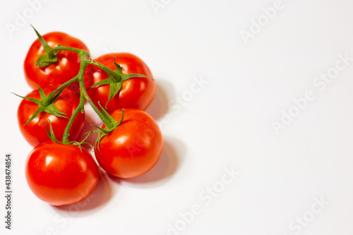 red organic tomatoes on a green branch on a white background © vadiar