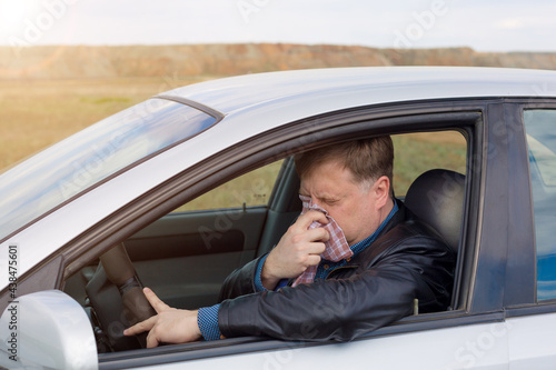 A man driving a car with a high temperature wipes his snot with a handkerchief.