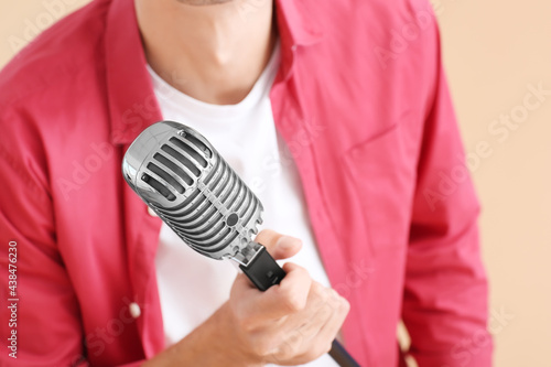 Young man with microphone on color background, closeup