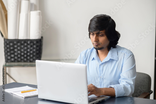 Indian man in smart casual shirt using laptop indoor, concentrated hindu male office employee typing, sends emails, working on a new project, researches the topic, develops strategies, websurfing