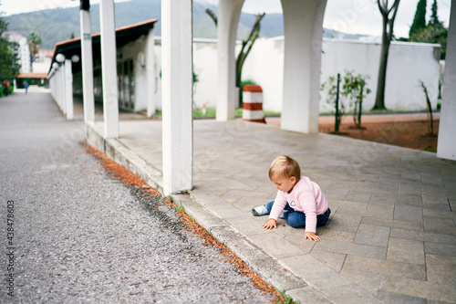 Little girl sits on a tile in a long pavilion in the park