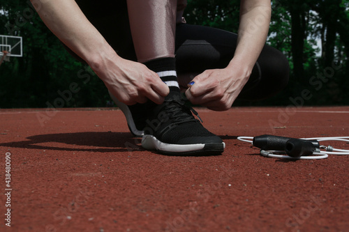 Running shoes. Woman tying shoelaces on the sport field. Runner getting ready for jogging.