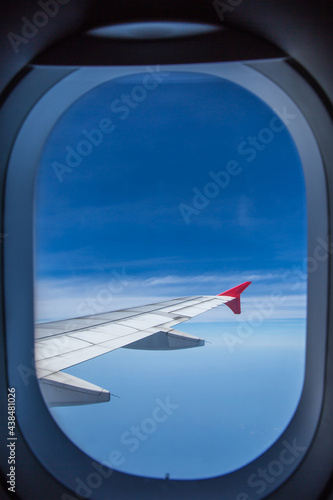 View from window of an airplane wing aircraft flying above the clouds in a blue sky.