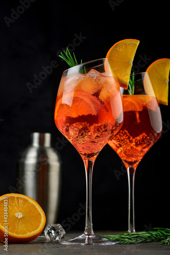 Wineglass of ice cold Aperol spritz cocktail served in a wine glass, decorated with slices of orange and rosemary branch. Black background