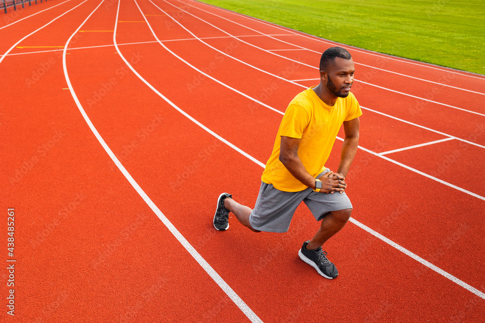 Obraz premium Portrait of sporty focused black man in sports wear warming up before training outdoors, wearing yellow trendy sportswear.Young Afro American stretching body at the stadium field