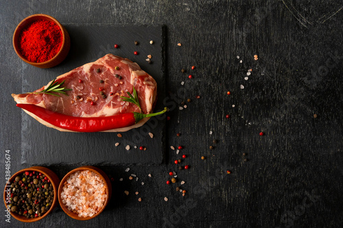 Raw piece of ribeye beef steak on slate board on a wooden table hot pepper smile, spice, himalayan salt, tomato. Fresh food. Everything for a barbecue.