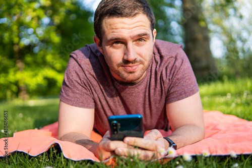 Photo of a young and attractive guy lying on a towel in the park checking his smartphone while enjoying a summer day outside. 