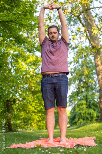 Obraz na płótnie Photo of a young and attractive man in the park streching with his arms up to the sky and his eyes closed. Alone in nature during a summer day. Yoga pose w salonie