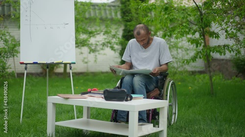 Concentrated disabled man analyzing business graphs on backyard outdoors. Portrait of focused African American male analyst in wheelchair examining paperwork thinking planning idea