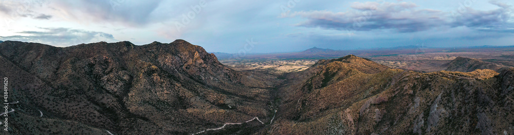 Aerial panoramic view of mountain ridges in Arizona and a valley with a dark blue sky and clouds and a roadway up.