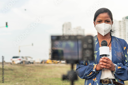 Black presenter in face mask speaking into microphone while standing in the city