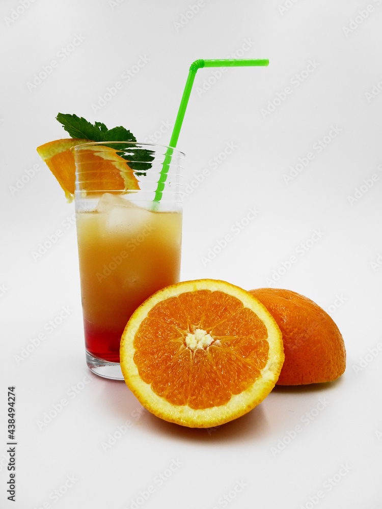 Non-alcoholic cocktail with orange juice ,cranberry juice ,ice cubes in a glass topped with a green straw ,mint and orange slice and an orange in the front on a white background Non-alcoholic cocktail with orange juice ,cranberry juice ,ice cubes in a glass topped with a green straw ,mint and orange slice and an orange in the front on a white background