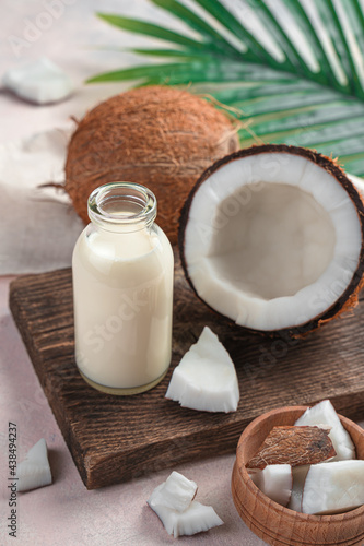 A bottle of milk and coconuts on a pink background with a palm leaf. Vertical view.