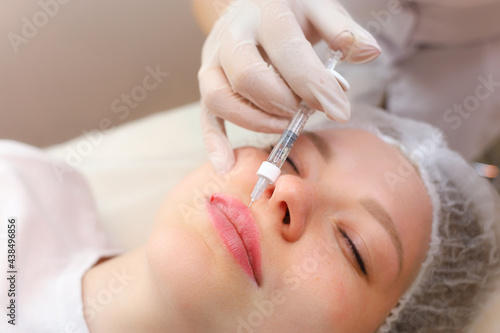 The girl is undergoing a lip augmentation procedure with a master cosmetologist who holds the lip edge with one finger and gives an injection of hyaluronic acid