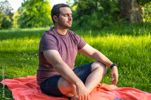 Photo of a young and attractive man sitting on a towel with his eyes closed and his legs crossed meditating in the middle of nature. Enjoying silence, relaxing with a guided meditation