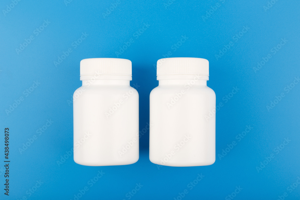 Two white plastic bottles of medicine on blue background. Concept of medical treatment of different diseases Two white plastic bottles of medicine on blue background. Concept of medical treatment of different diseases