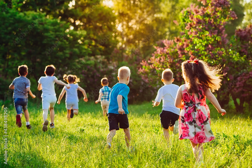 Fototapeta premium A group of happy children of boys and girls run in the Park on the grass on a Sunny summer day.