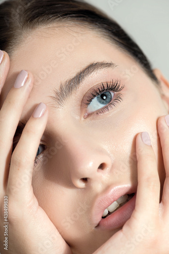 Beautiful young woman with clean perfect skin. Portrait of beauty model with natural nude make up and and hand with manicure touching face. Spa, skincare and wellness. Close up
