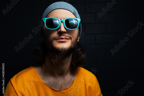 Portrait of young smiling man on black background, wearing blue sunglasses and orange shirt. © Lalandrew