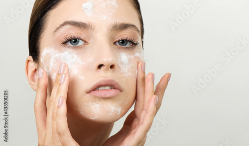 Beautiful young girl cleansing face with cosmetic facial skincare foam, gel or soap. Woman hame SPA procedures photo