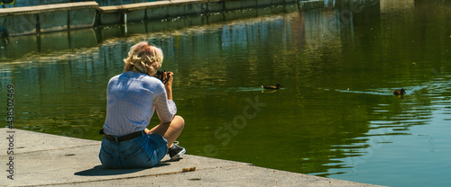 mujer sentada al lado de un lago haciendo fotos a los patos con su cámara réflex  , mujer joven con blusa blanca y pantalones cortos azules sujetando una cámara de fotos photo
