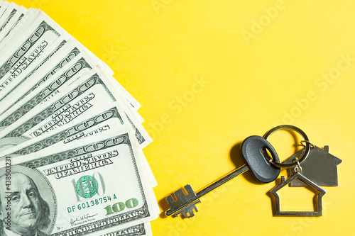 Home key with a keychain on a stack of $ 100 bills on yellow background. Purchase of an apartment, house, real estate, business, mortgage and housing loan from bank, savings, cash, moving. Copy space