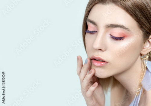 Beautiful young woman with clean perfect skin and blue-pink makeup and feather earings. Portrait of beauty model with natural make up and long eyelashes.