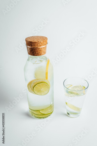Refreshing glass of water, a bottle with a slice of lemon and lime inside on white background