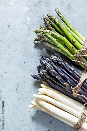 Raw white, purple, green asparagus on a blue background. Raw food concept.