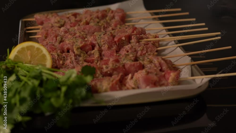 4K slide by clip of raw marinated pork skewers (Souvlaki) on parchment lined baking sheet ready to be grilled. Lemon and cilantro on the side. Indoors, kitchen, series. 4K slide by clip of raw marinated pork skewers (Souvlaki) on parchment lined baking sheet ready to be grilled. Lemon and cilantro on the side. Indoors, kitchen, series.