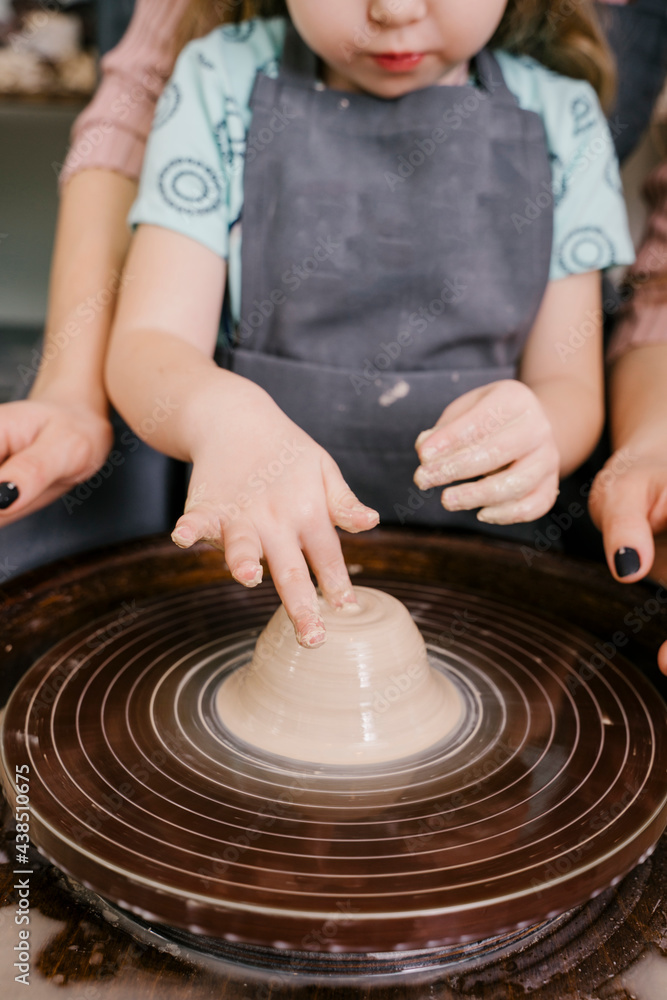 Woman helping girl to mold mass in pottery wheel