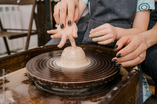 Woman helping girl to mold mass in pottery wheel photo
