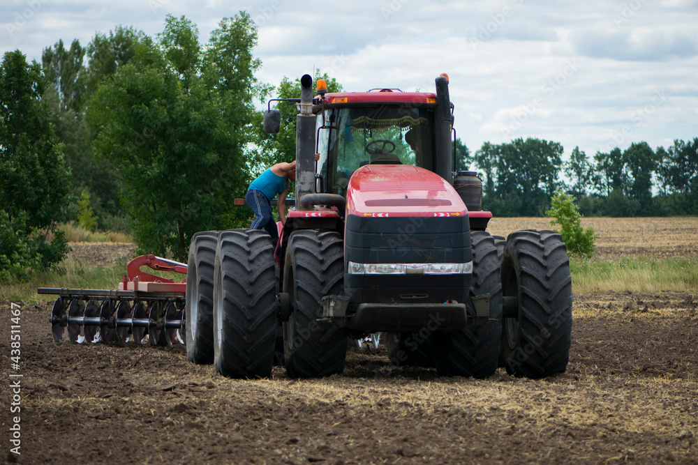 tractor driver near a large red tractor. A farmer on a tractor prepares land for a seeding tractor with a plow in an agricultural field. August, Ukraine tractor driver near a large red tractor. A farmer on a tractor prepares land for a seeding tractor with a plow in an agricultural field. August, Ukraine