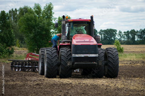 tractor driver near a large red tractor. A farmer on a tractor prepares land for a seeding tractor with a plow in an agricultural field. August, Ukraine