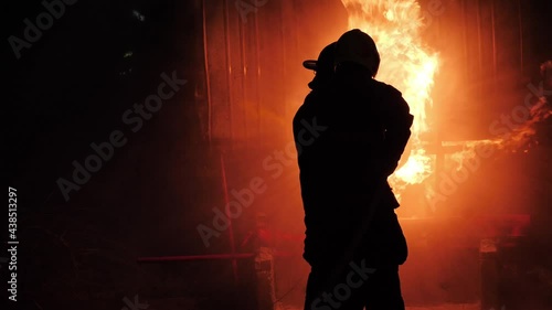 Rear view of Asian fireman wear fire protection suit. Firefighter in full gear operating a fire hose at Fire station at night. Training fire drill Slow motion photo