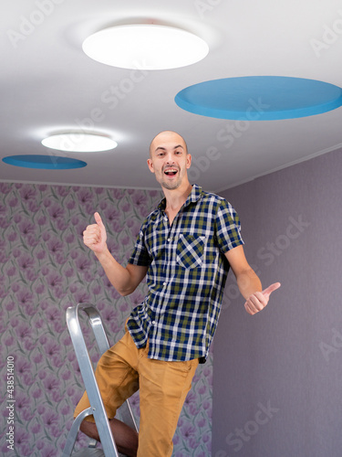 The man on the stepladder replaced the led light on the ceiling and is happy with the work done.